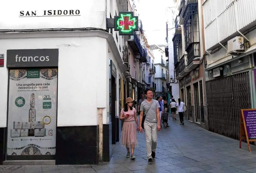 Una pareja camina junto a una c&eacute;ntrica farmacia en Sevilla. - AI