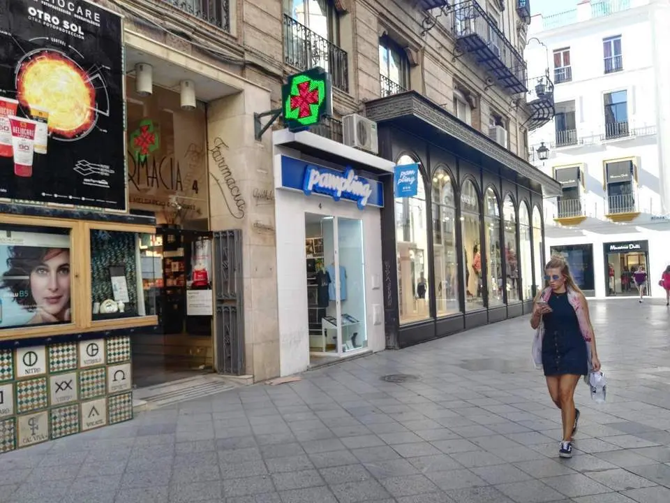 Una joven pasa ante una farmacia en una c&eacute;ntrica calle de Sevilla. - AI