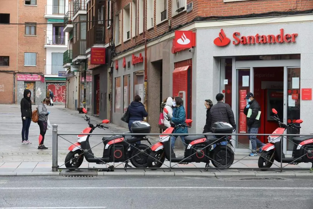 Varias personas esperan ante la puerta de una oficina del Santander. - EP