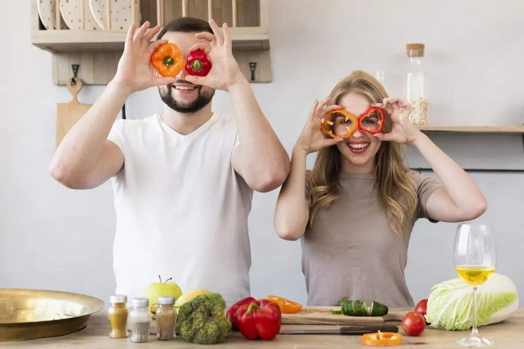 Pareja sonriente con pimientos en la cocina. - Freepik