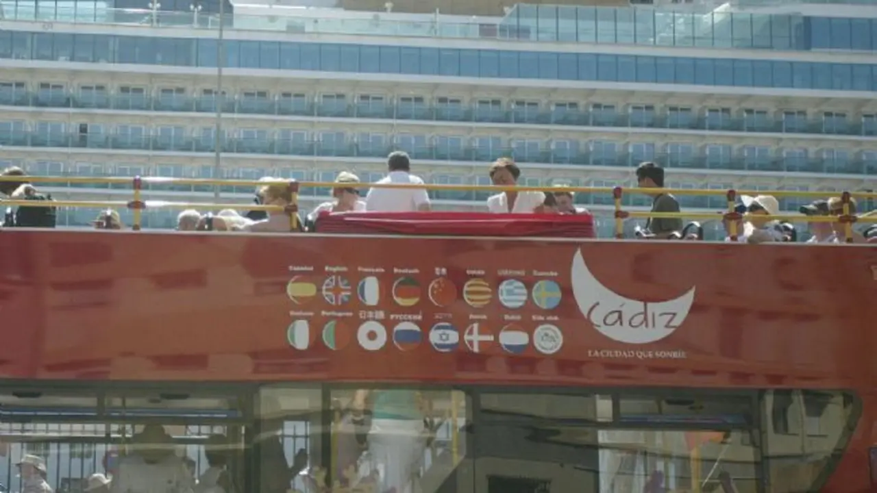 Varios visitantes, a bordo de un autob&uacute;s tur&iacute;stico, pasan junto a un crucero amarrado en el puerto de C&aacute;diz. - IJ Poveda