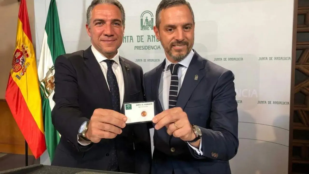 Juan Bravo (derecha) con una de las tarjetas junto al portavoz del Gobierno, El&iacute;as Bendodo. - Junta
