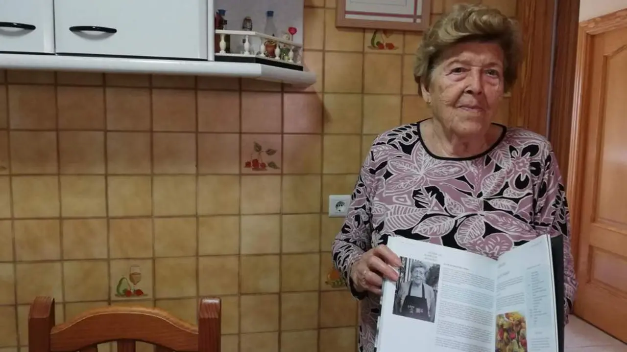 Juana Alarc&oacute;n en la cocina de su casa con el libro en el que aparece su receta. - A.M.