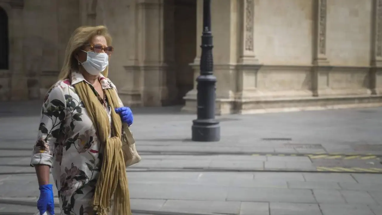 Una mujer caminando protegida con mascarilla y guantes. - EP