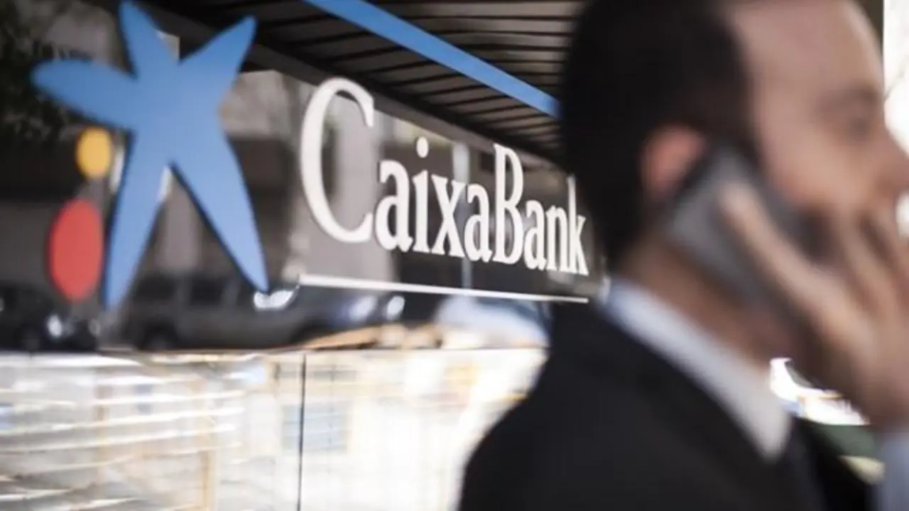 Un hombre usa un tel&eacute;fono m&oacute;vil junto a una oficina de CaixaBank. - EP