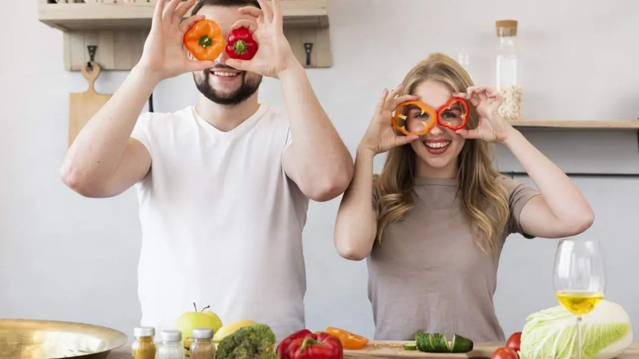Pareja sonriente con pimientos en la cocina. - Freepik