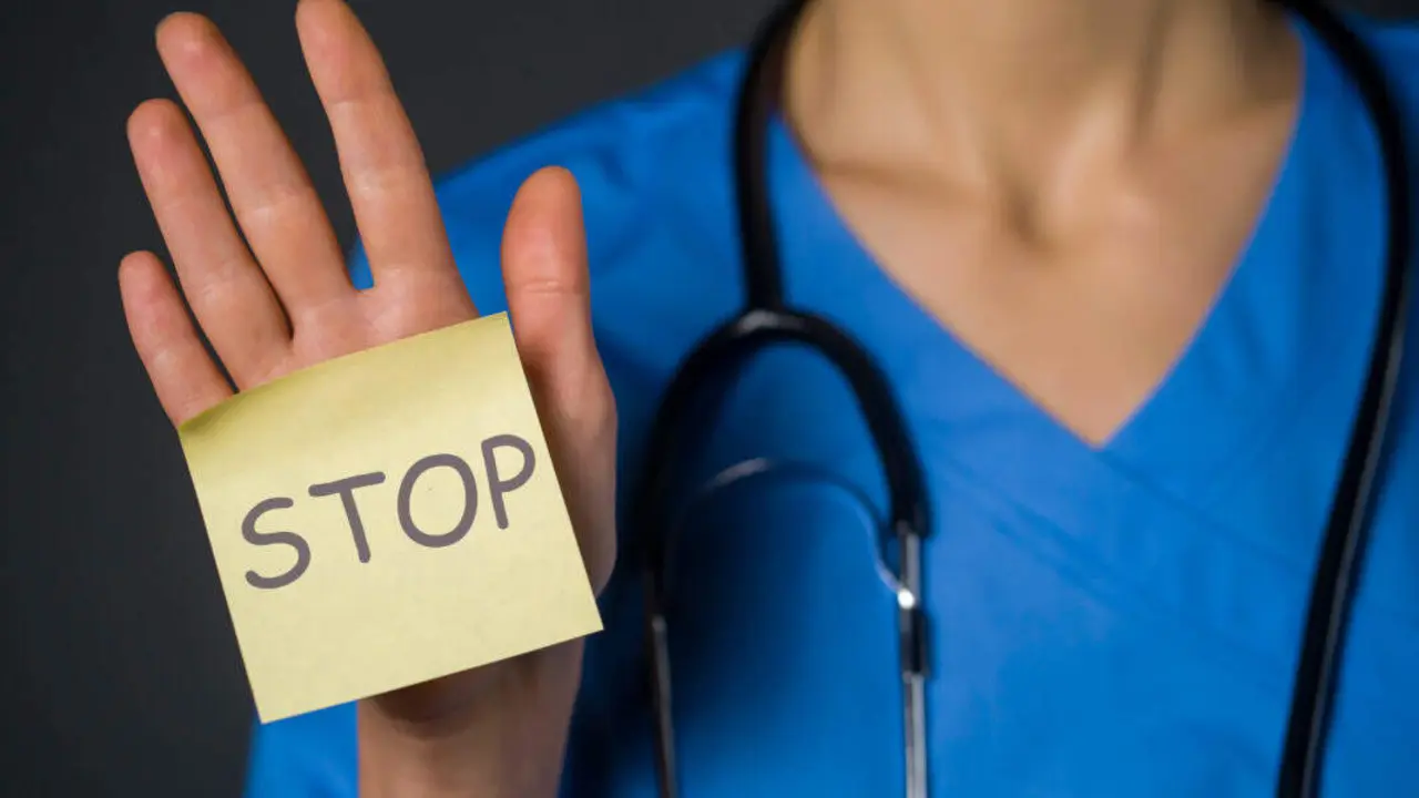 A woman doctor holds a paper in her palm, a note with the inscription "stop" in her hand. A young nurse in a medical suit and with a stethoscope transmits a message