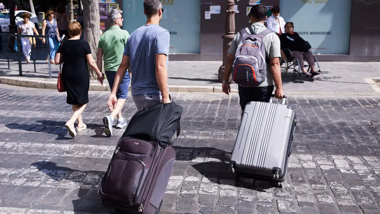 Dos turistas, con maletas, cruzan un paso de peatones en Sevilla. | Archivo